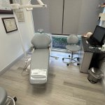 Dental treatment room with patient chair, overhead dental equipment, light flooring, and clinical furnishings