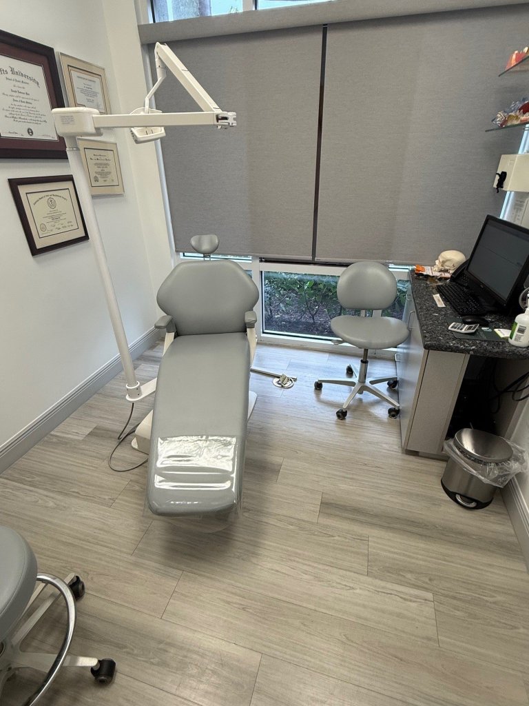 Dental treatment room with patient chair, overhead dental equipment, light flooring, and clinical furnishings