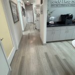 Interior hallway showing light wood flooring throughout, view into reception area with desk, bright and modern design
