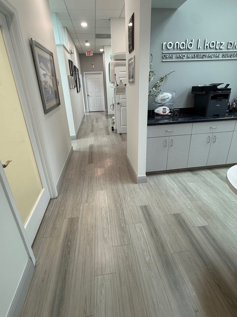 Interior hallway showing light wood flooring throughout, view into reception area with desk, bright and modern design