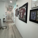 Corridor with framed artwork on white walls, light colored flooring, and clean professional medical office aesthetic