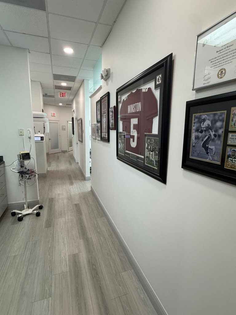 Corridor with framed artwork on white walls, light colored flooring, and clean professional medical office aesthetic