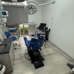 Dental operatory with blue patient chair, ceiling-mounted dental delivery system, equipment, and modern clinical setup