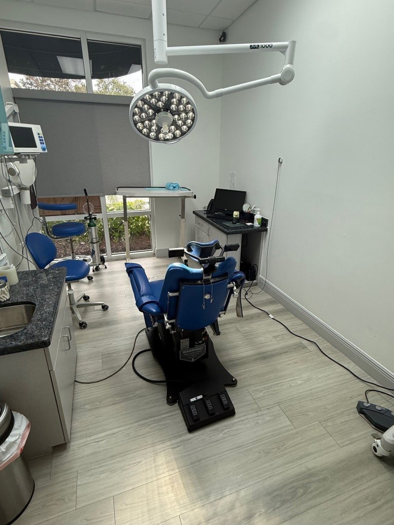 Dental operatory with blue patient chair, ceiling-mounted dental delivery system, equipment, and modern clinical setup