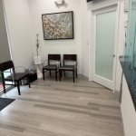 Waiting area with black chairs, framed artwork on wall, light wood flooring, and glass door entrance