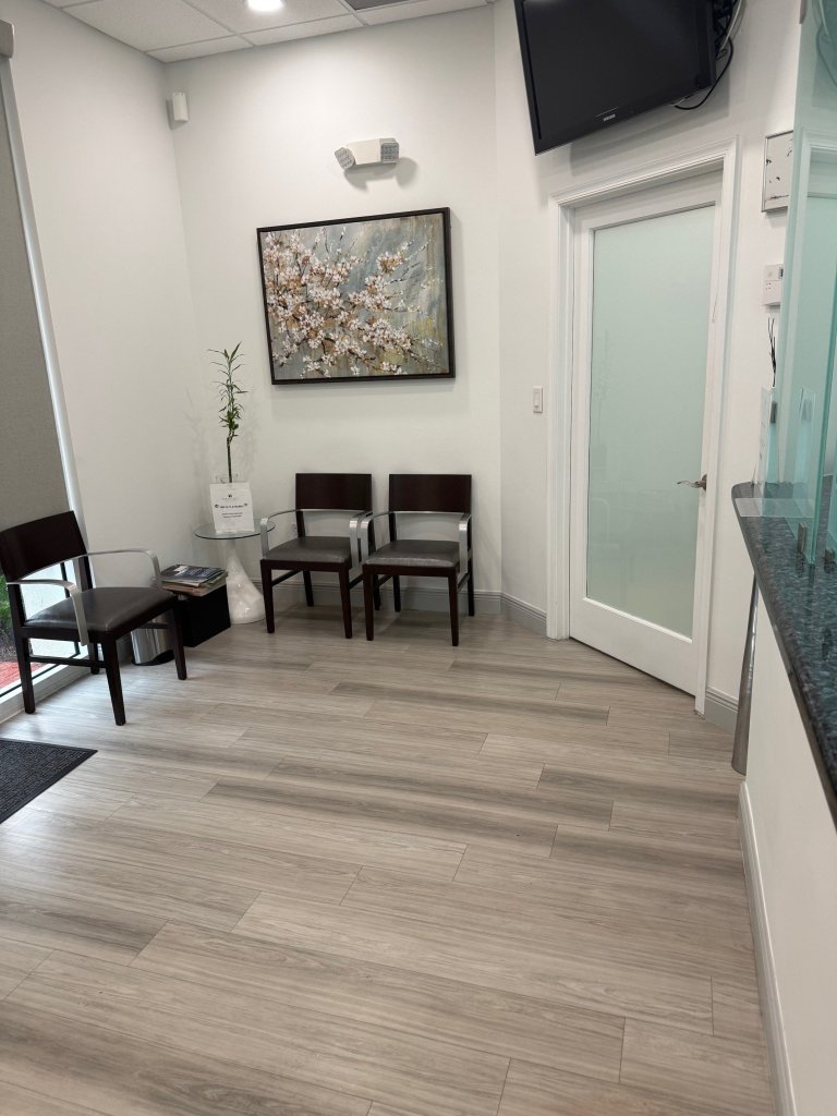 Waiting area with black chairs, framed artwork on wall, light wood flooring, and glass door entrance