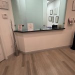 Reception area with glass-enclosed office space, light wood flooring, and neutral beige walls in modern dental office