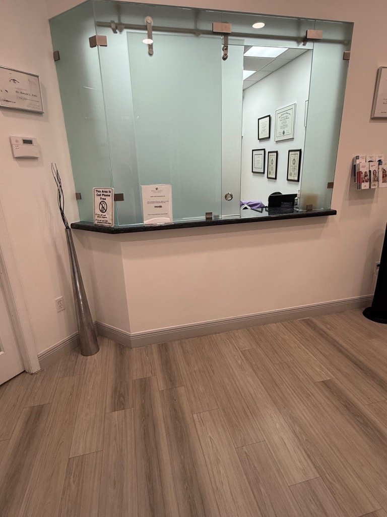 Reception area with glass-enclosed office space, light wood flooring, and neutral beige walls in modern dental office