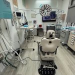 Dental operatory with beige patient chair, ceiling-mounted surgical light, wall cabinets, and comprehensive dental equipment setup