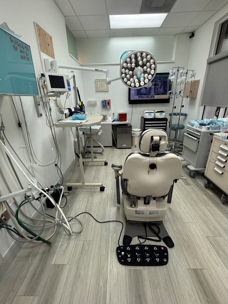 Dental operatory with beige patient chair, ceiling-mounted surgical light, wall cabinets, and comprehensive dental equipment setup