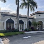 Exterior view of Mediterranean-style medical/dental office building with white stucco walls, terracotta roof tiles, arched windows and entryways, surrounded by palm trees and professional landscaping